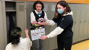 Student slates two actors, dressed formally, in front of lockers